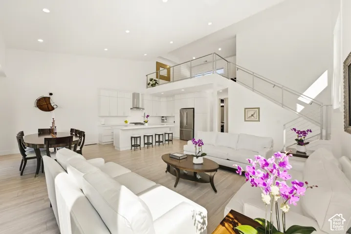 Open-concept living space with light wood-finish flooring, a contemporary kitchen, and a staircase featuring stainless steel railings