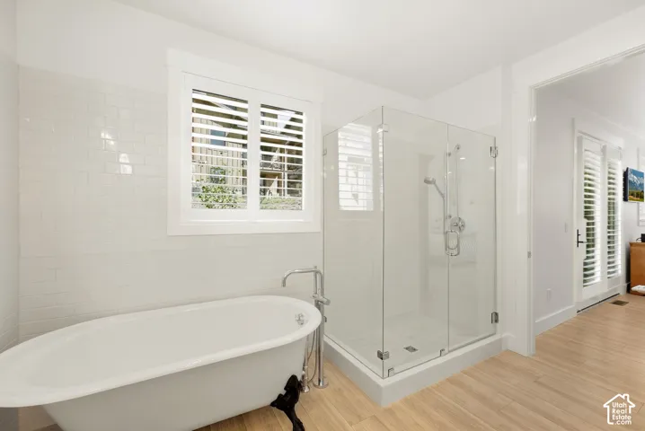 Freestanding clawfoot tub with floor-mounted faucet, glass-enclosed shower, white subway tile surround, and wood-finish flooring