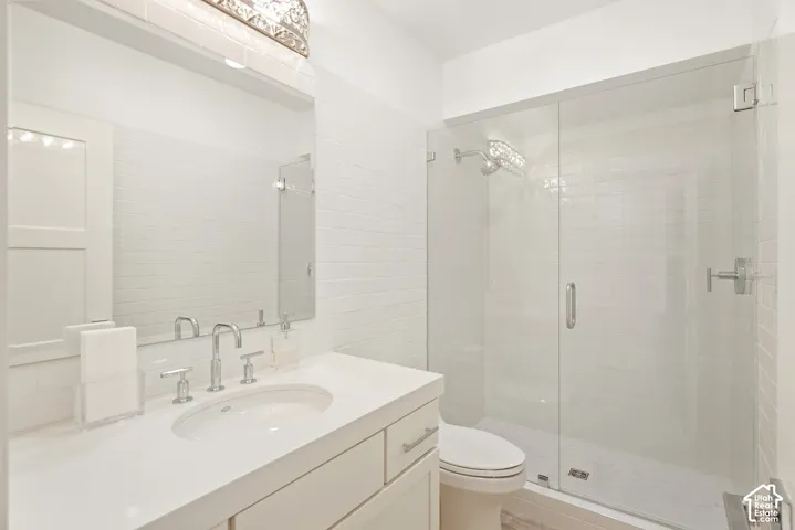 White vanity with an integrated sink, brushed nickel fixtures, subway tile wall, and a glass-enclosed shower