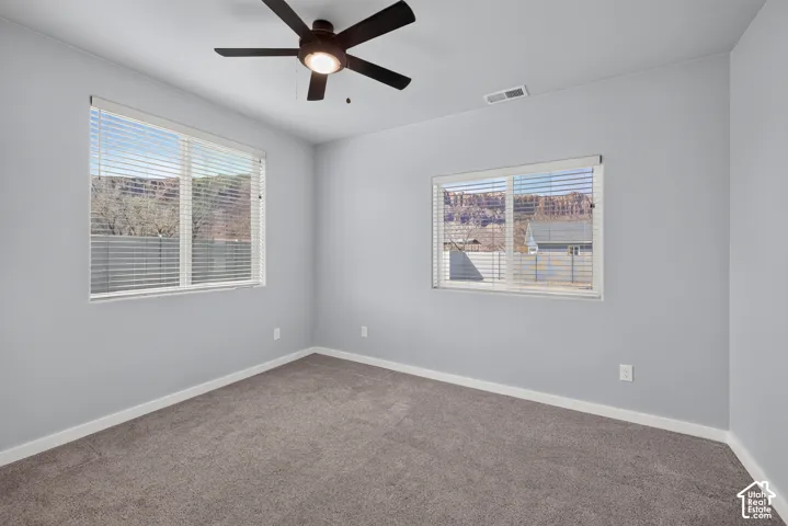 Carpeted room featuring multiple windows, a ceiling fan, and light gray walls