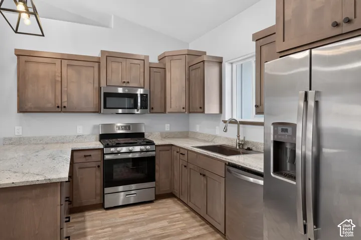 Kitchen featuring wood-finish cabinetry, light-toned countertops, stainless steel appliances, and a stainless steel sink with a gooseneck faucet