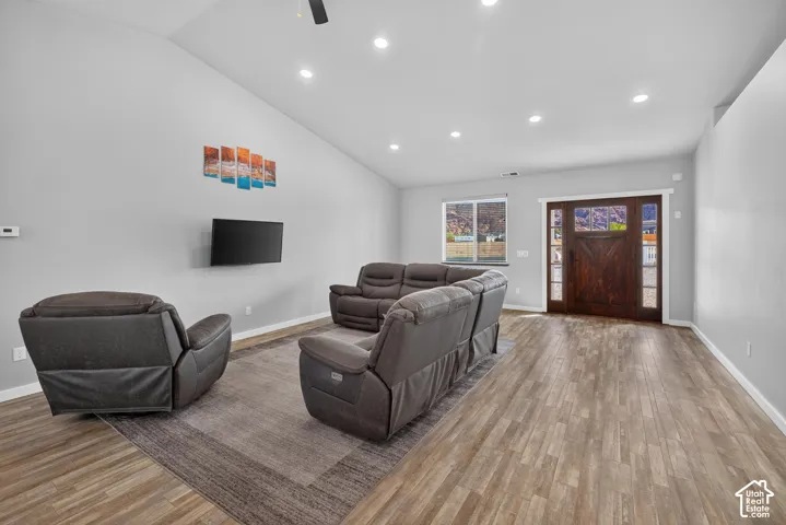 Vaulted ceilings with recessed lighting, wood-finish flooring, a dark wood-finish entry door with clear glass panels, and a large window providing natural light