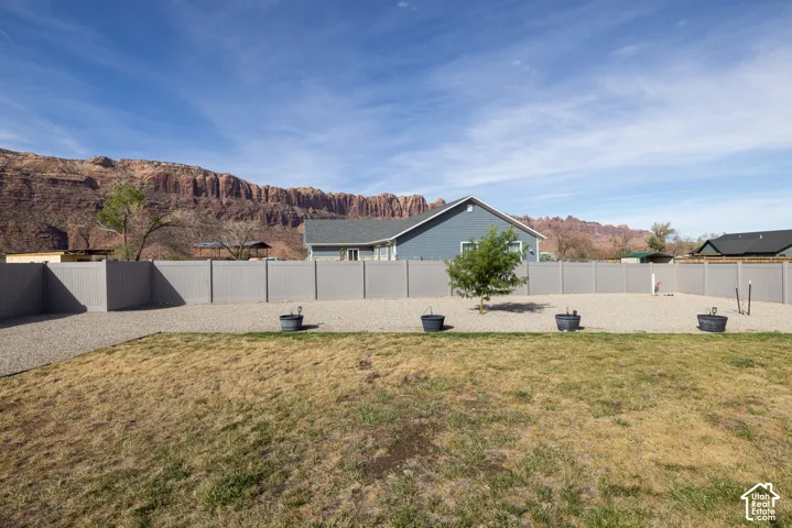 Expansive outdoor area featuring a gravel and grass surface, a full privacy fence, and a distant mountain backdrop