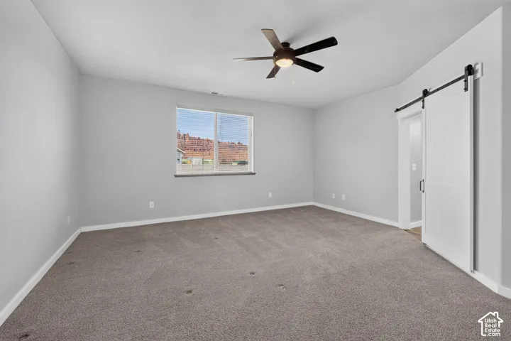 Carpeted room featuring a ceiling fan, a window with horizontal blinds, and a white barn door
