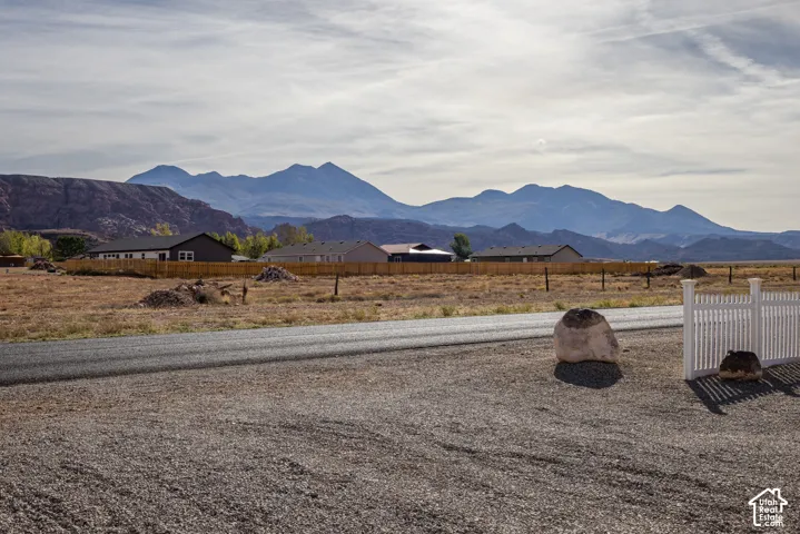 Expansive lot featuring a gravel and paved road, white picket fence, and distant mountain range