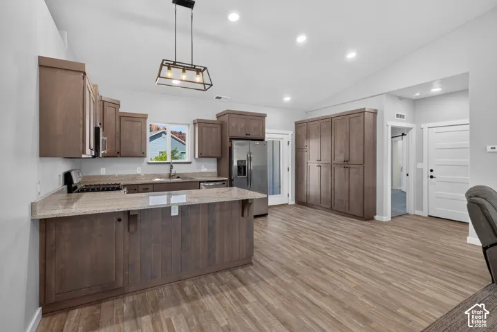 Vaulted ceiling with recessed lighting, wood-finish flooring, full-height cabinetry, stainless steel appliances, and a kitchen island with stone countertops