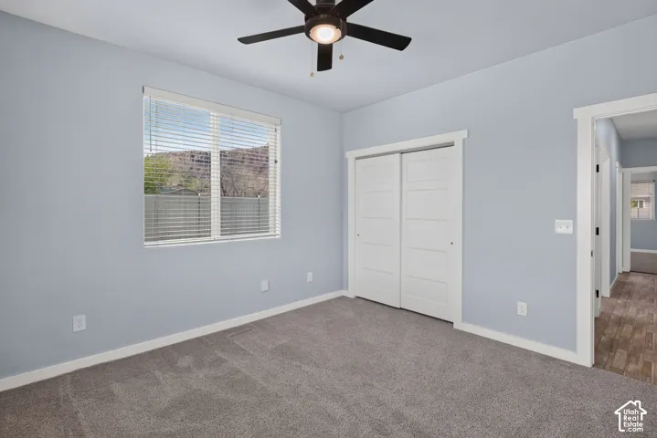 Carpeted flooring, window with blinds, ceiling fan with light fixture, white trim, and sliding closet doors