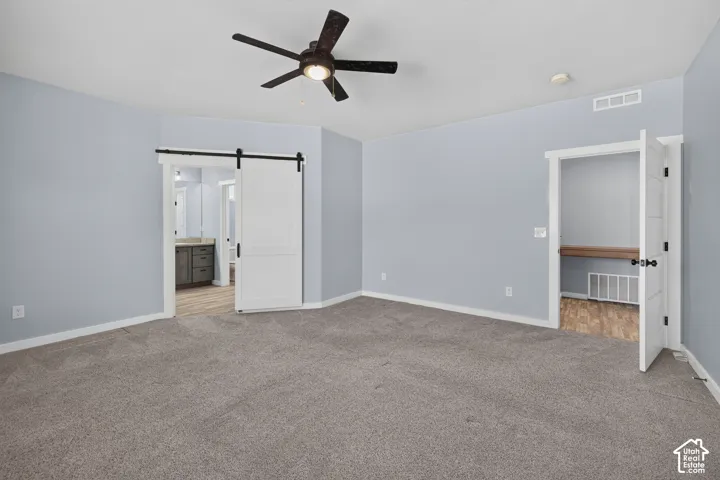 Gray carpet flooring, ceiling fan, white barn door, built-in shelving, and light blue wall paint