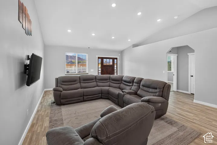 Vaulted ceiling, recessed lighting, wood-finish flooring, white trim, and a paneled entry door