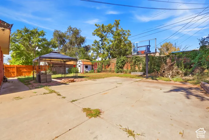 Expansive concrete patio with a freestanding basketball hoop, wood privacy fencing, and a detached storage shed