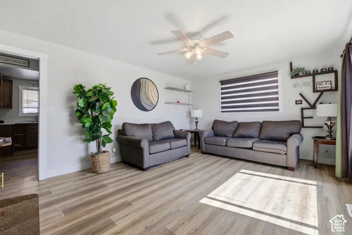 Wood-finish flooring, ceiling fan with light fixture, window with horizontal blinds, and a doorway to an additional room