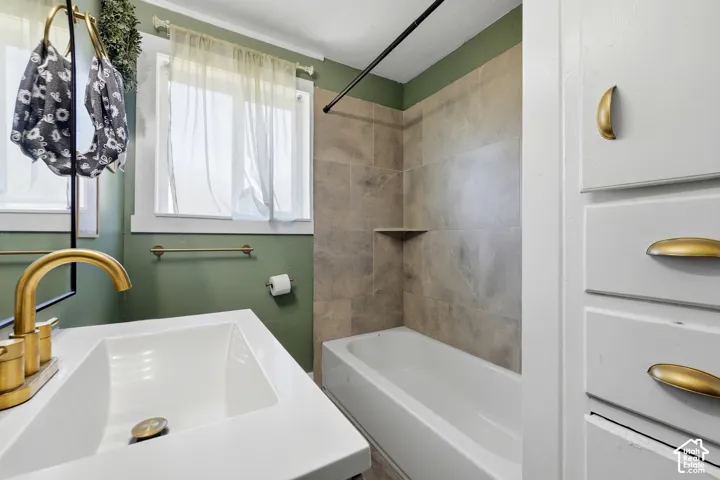 Bathroom featuring a white integrated sink, brass-finish faucet, subway tile shower surround with a built-in niche, and a window with white trim