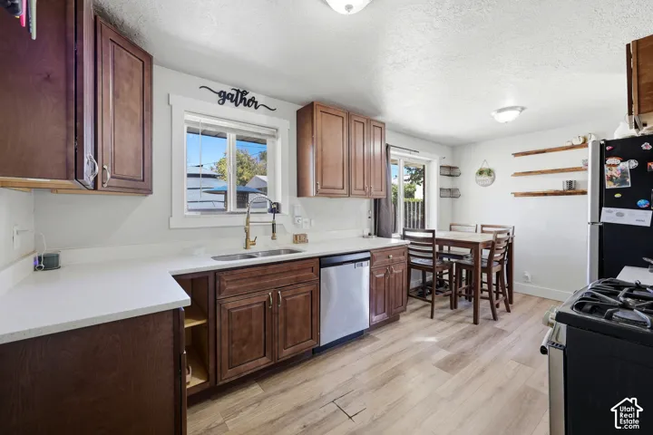 Kitchen featuring wood-finish flooring, wood cabinetry, white countertops, stainless steel sink, and a stainless steel dishwasher