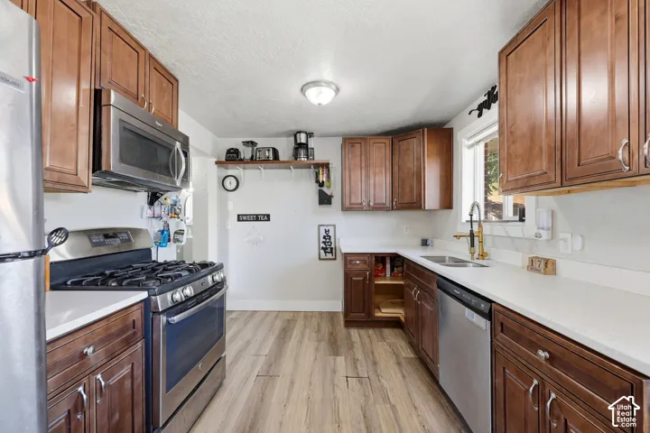 Wood-finish flooring, white countertops, dark wood cabinetry, stainless steel appliances, and a gold-finish faucet