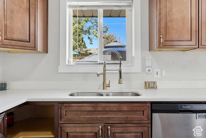 White countertop with an undermount double-basin stainless steel sink, bronze-finish faucet, and coordinating dark wood-finish cabinetry