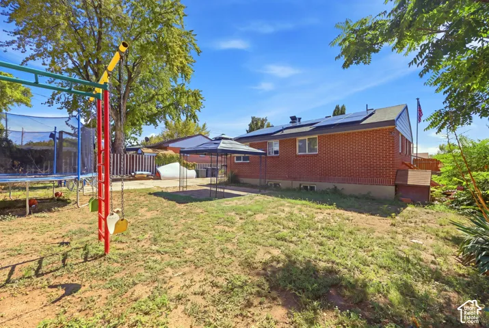 Brick exterior, dark roof, multiple solar panels, and a small built-in shed