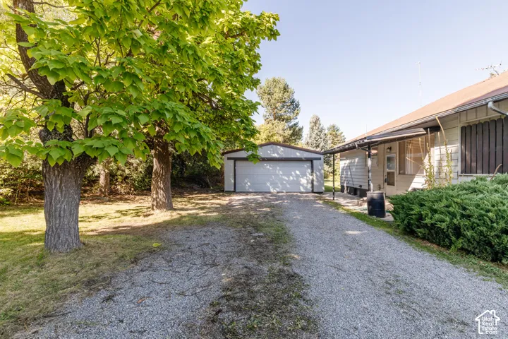 Gravel driveway with a detached garage structure and mature trees