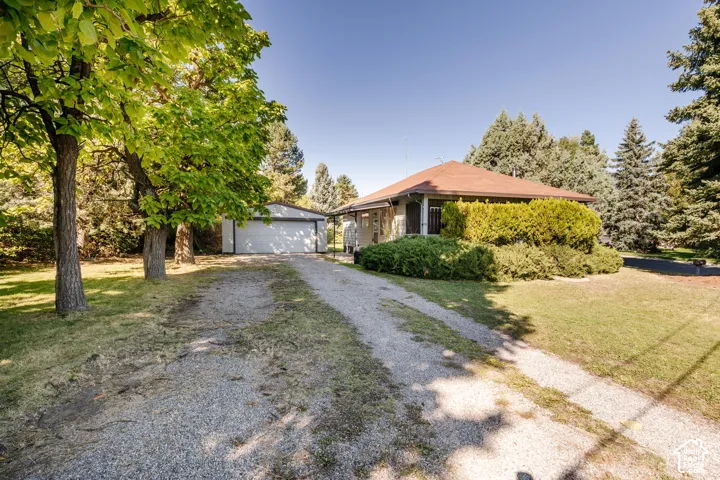 Gravel driveway leading to a detached garage and a single-story home with a hip roof and established perimeter landscaping