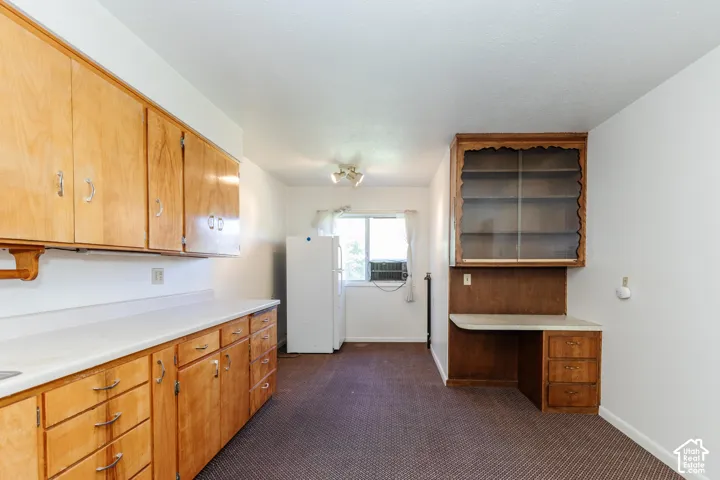 Kitchen featuring wood cabinetry, white countertops, built-in desk, and display shelving
