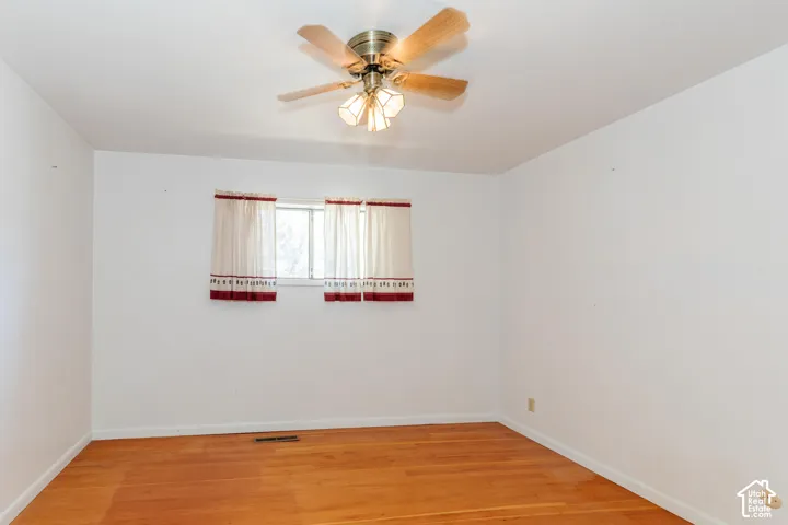 Hardwood-style flooring, white painted walls, window with a light-filtering curtain, and a ceiling fan with integrated lighting