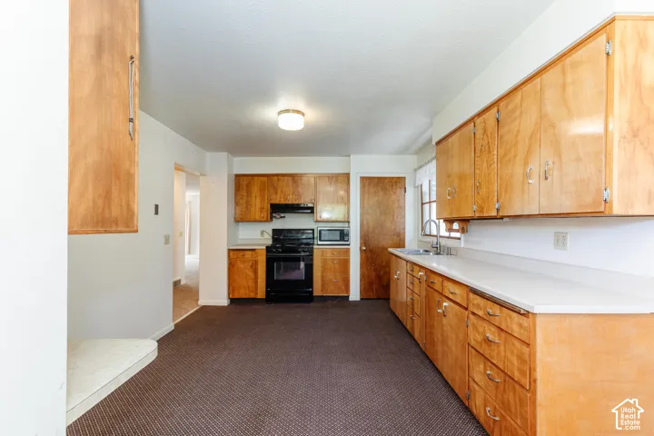 Wood cabinetry, light-toned countertops, stainless steel sink, black range, and built-in microwave