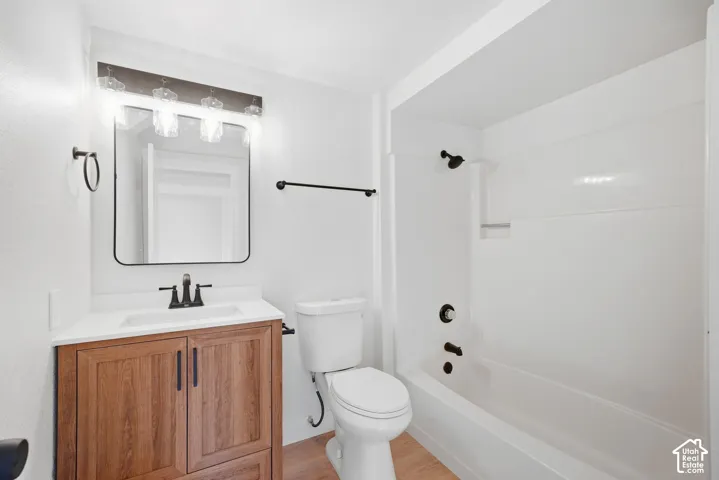 Wood-finish flooring, white vanity with integrated sink, black-framed mirror, and a white tub/shower combination with matte black fixtures