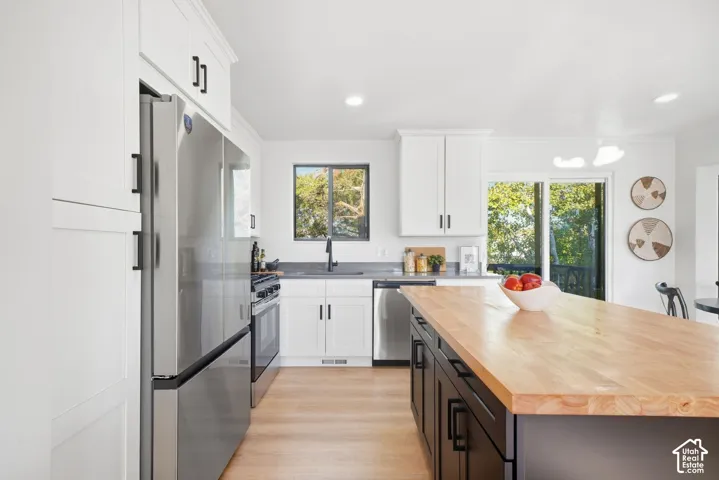 Modern kitchen featuring stainless steel appliances, a large wood-finish island, white cabinetry, and wood-finish flooring