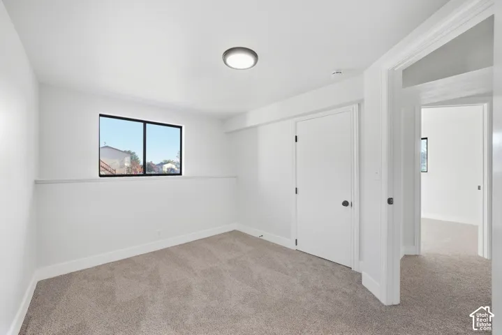 Neutral tone wall paint, carpet flooring, a window with dark framing, and a flush-mount ceiling light fixture