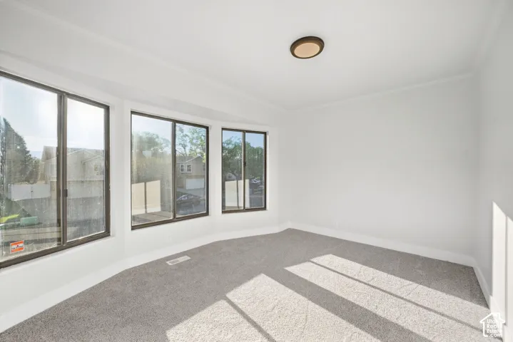 Bay window with multiple large panes, white painted walls, crown molding, and gray carpeting