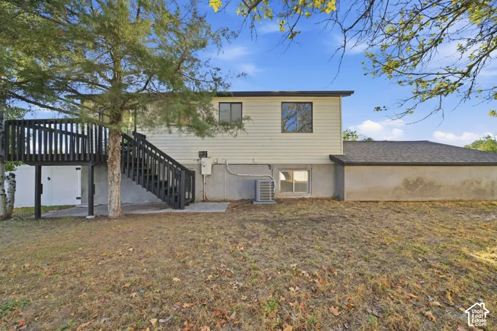 Expansive backyard featuring a multi-level deck with black railing, concrete patio, and mature trees