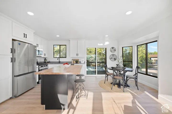 White cabinetry, a center island with a wood-finish countertop, stainless steel appliances, and wood-finish flooring