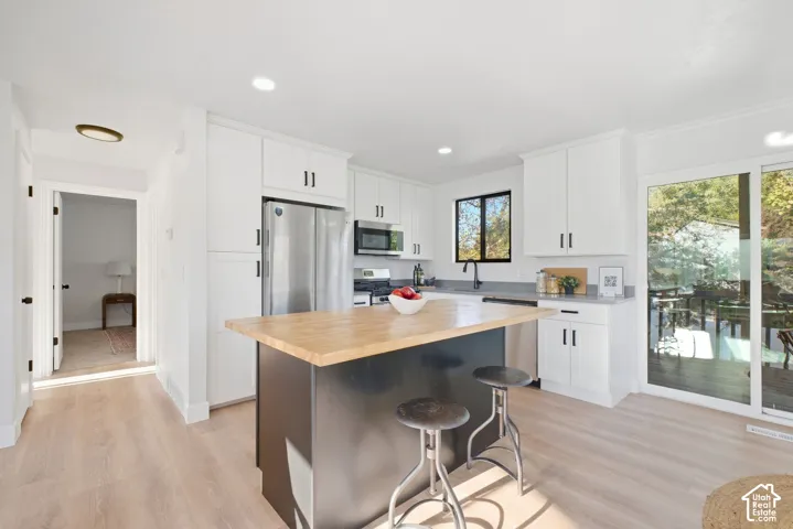 Modern kitchen featuring white cabinetry, stainless steel appliances, light wood-finish flooring, a central island with a wood countertop, and sliding glass doors