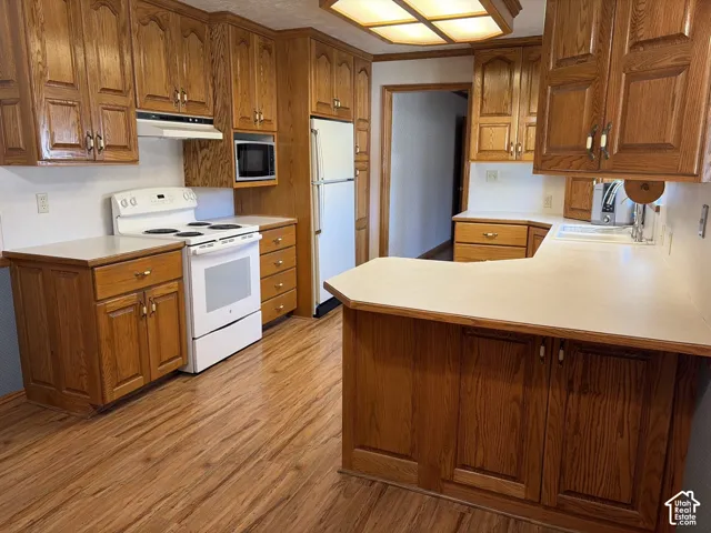 Kitchen featuring wood-finish flooring, wood cabinetry, white countertops, and white appliances
