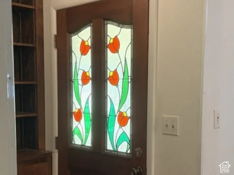 Entry door with decorative stained glass panels, wood-finish flooring, and built-in wood cabinetry