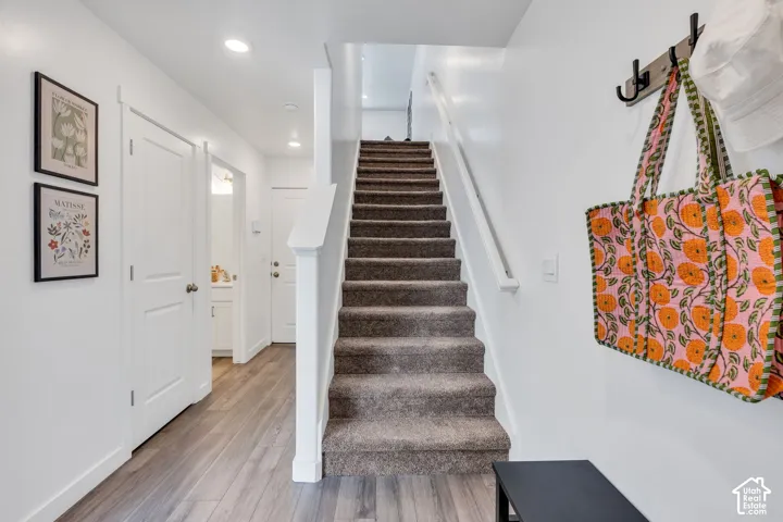 Carpeted staircase with white handrail, wood-finish flooring, recessed lighting, and white doors