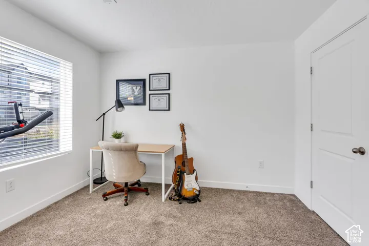Carpeted room with a large window featuring blinds, a white paneled door with dark hardware, and clean white walls