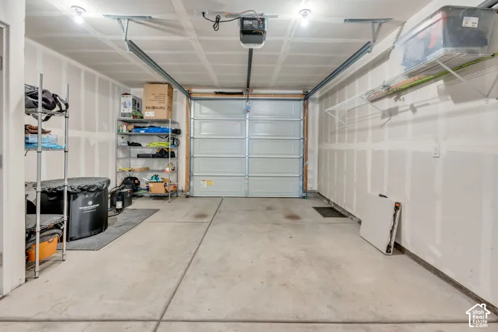 Concrete flooring garage with exposed drywall, overhead lighting, and built-in shelving