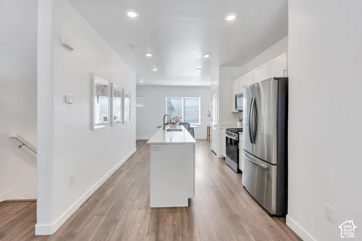 Open-concept kitchen with a central island, recessed lighting, wood-finish flooring, and stainless steel appliances