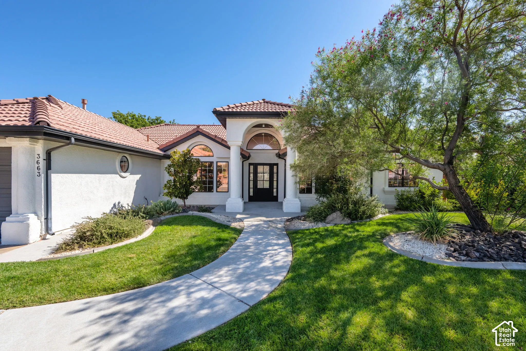 Stucco exterior with a tile roof, an arched entryway, a concrete pathway, and mature landscaping