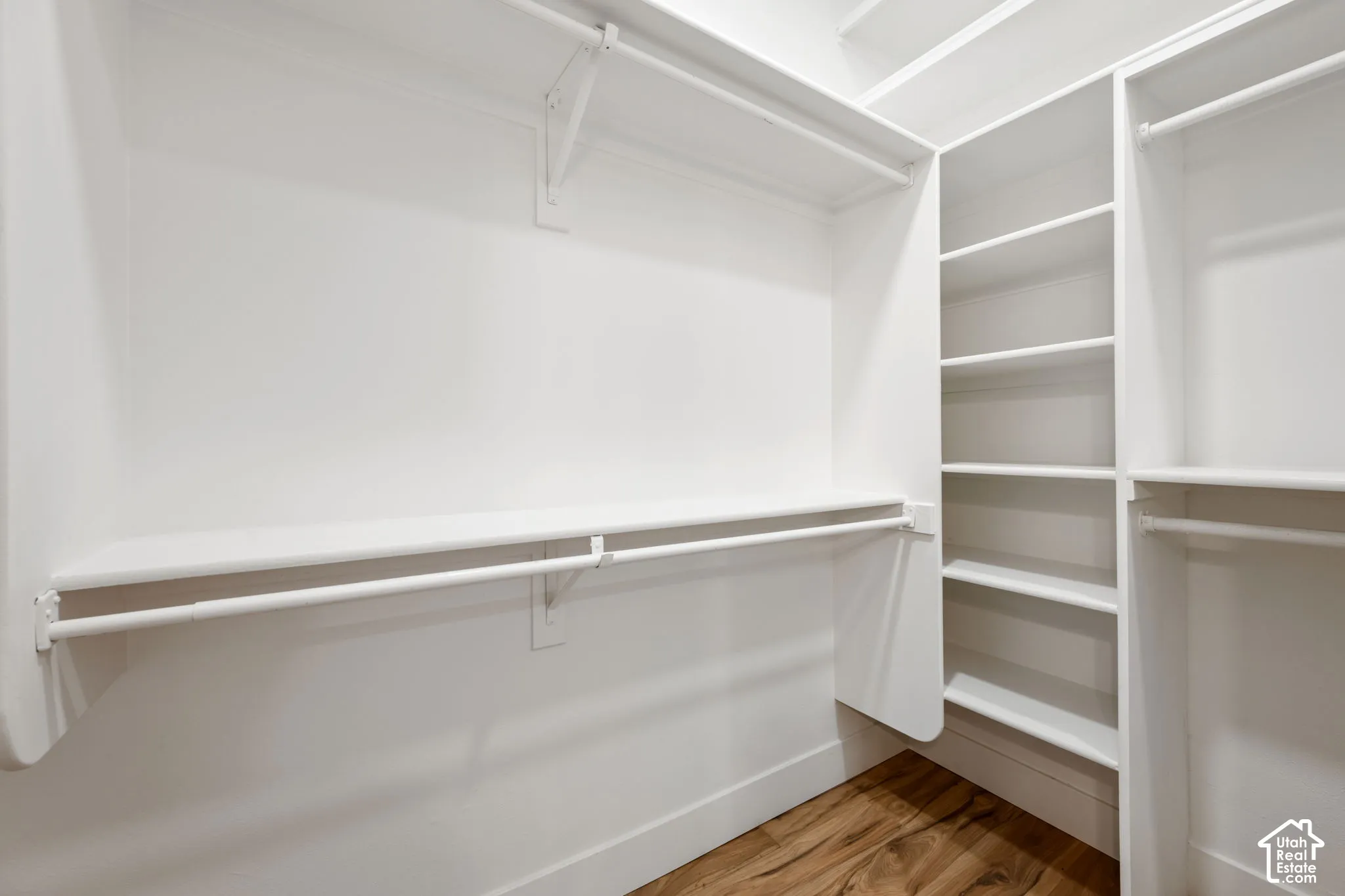 Built-in closet system featuring multiple shelves and hanging rods, white finishes, and wood-finish flooring