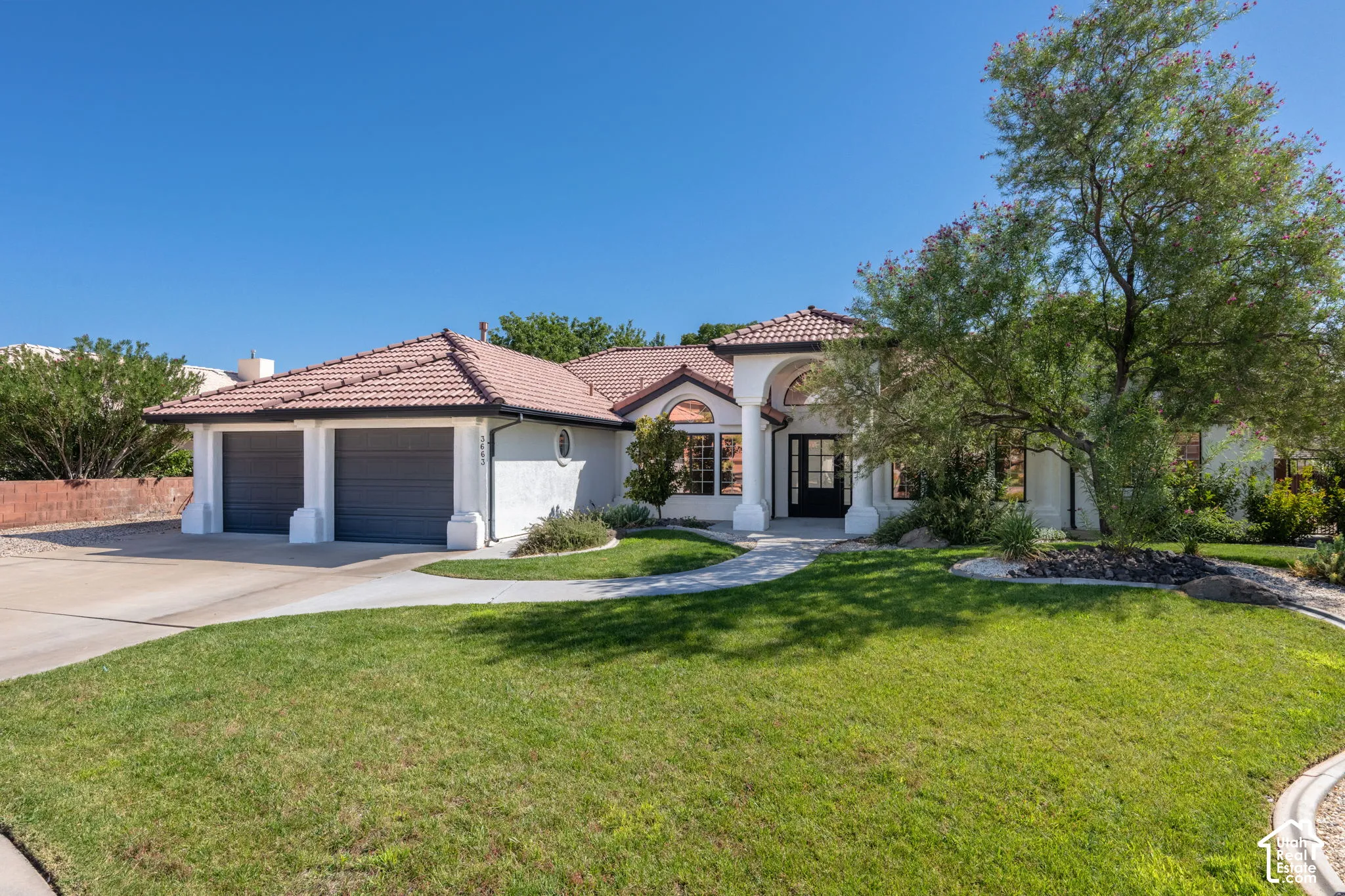 Stucco exterior with a tile roof, arched entry, two-car garage, and a curved concrete driveway