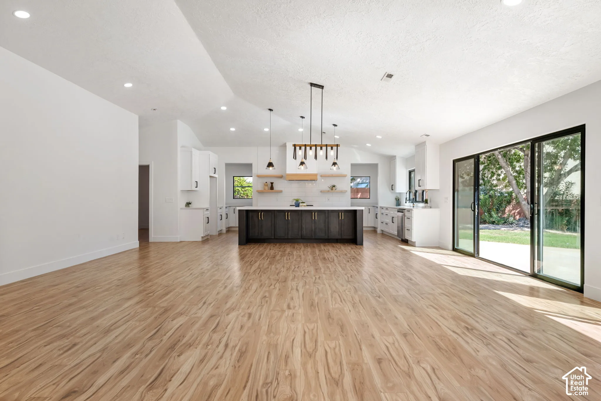 Wood-finish flooring throughout, vaulted ceilings, recessed lighting, modern kitchen island with pendant lighting, and multi-panel sliding glass doors