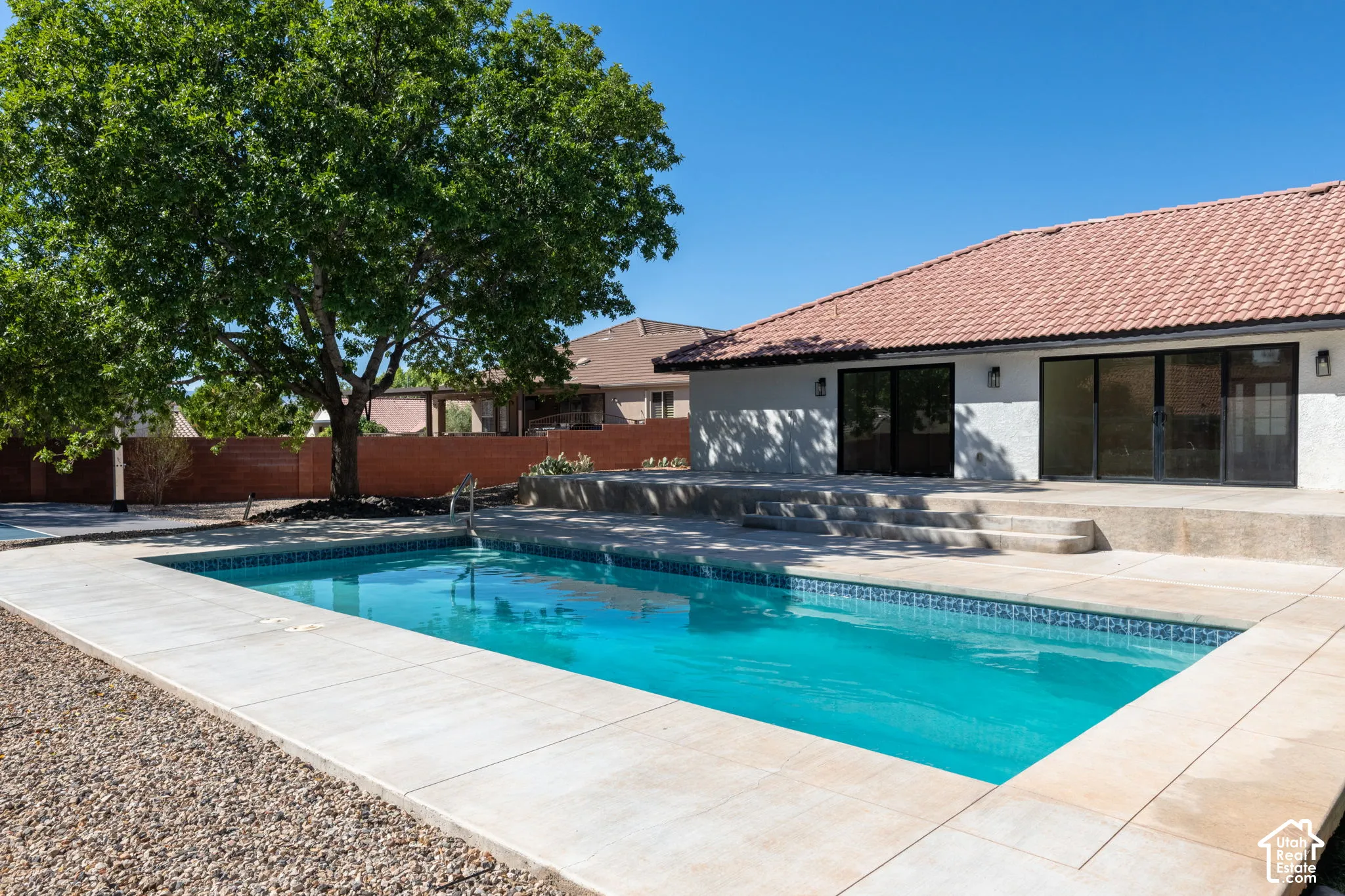 Rectangular swimming pool with tiled coping, surrounding concrete patio, and mature tree