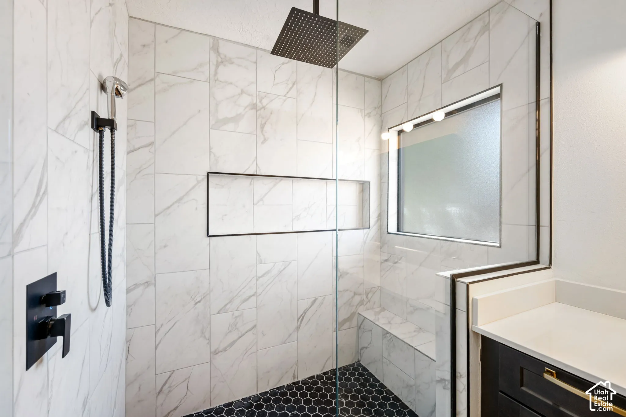 Walk-in shower featuring a built-in bench, black hexagon tile flooring, and a recessed niche