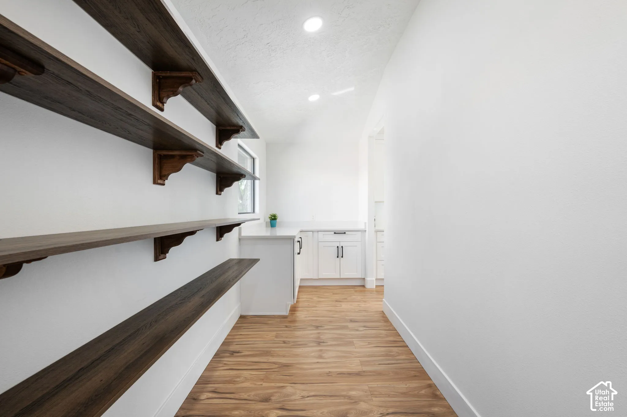 Wood-finish shelving with decorative brackets, light wood-finish flooring, recessed lighting, white cabinetry, and a countertop surface