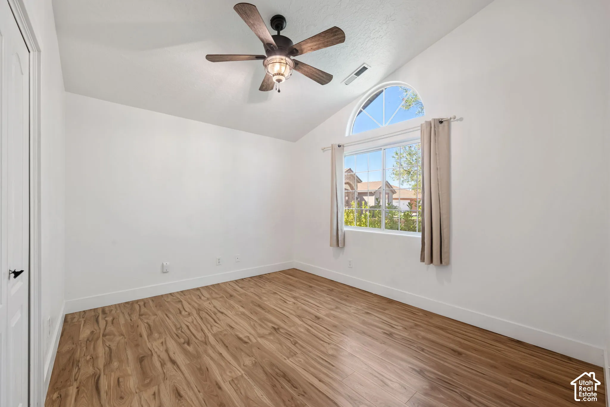 Vaulted ceiling with wood-finish ceiling fan, arched transom window, wood-finish flooring, and white walls