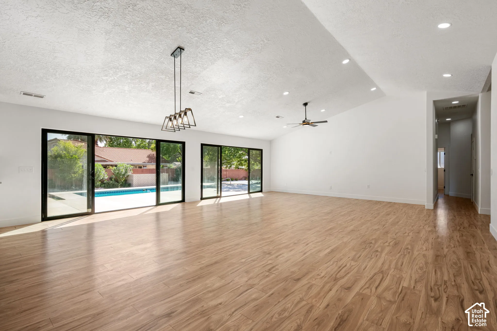 Wood-finish flooring throughout, vaulted ceiling, recessed lighting, and multiple sliding glass doors opening to an outdoor pool
