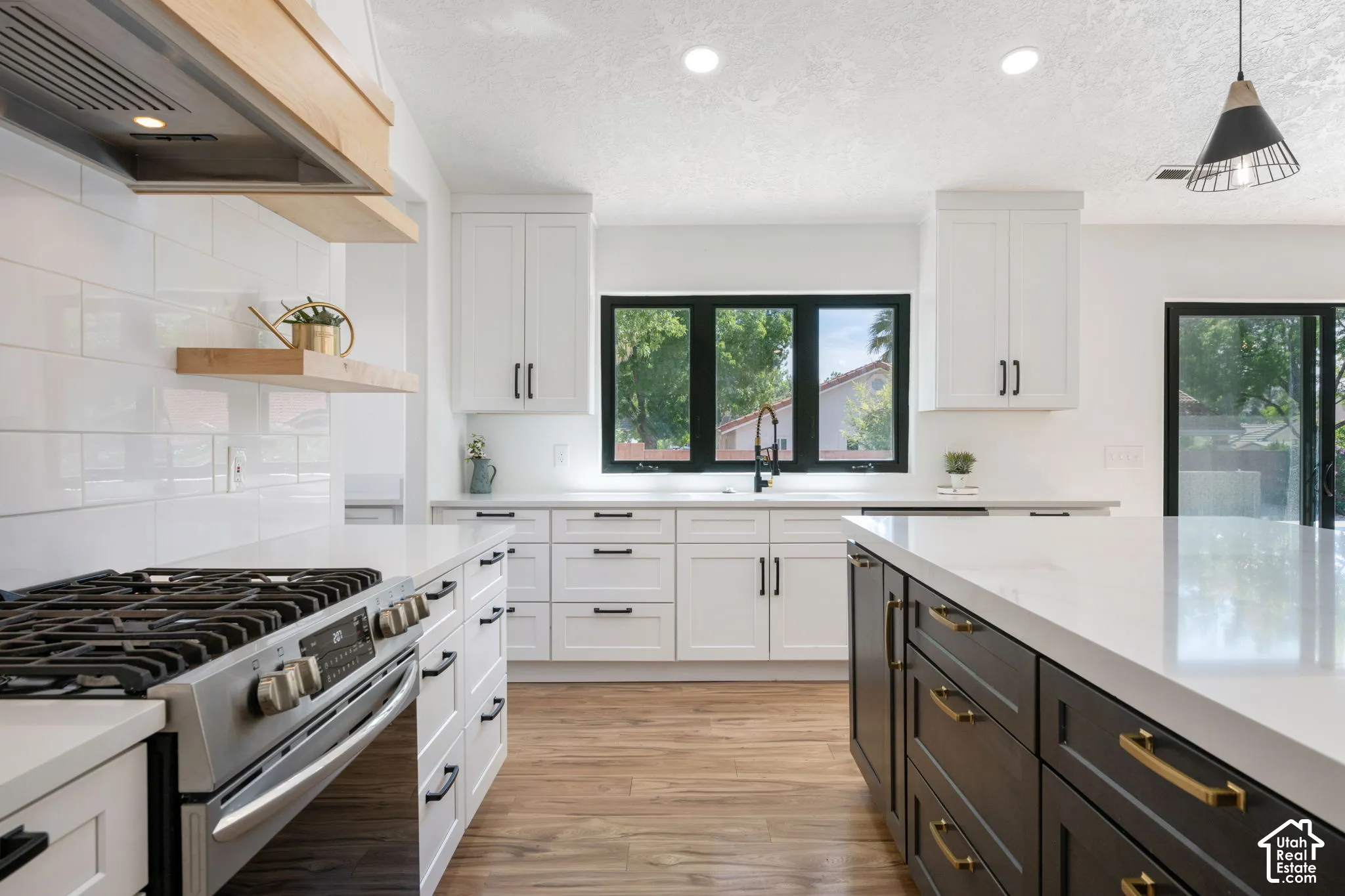 Gourmet kitchen featuring white shaker cabinetry, an expansive island with dark wood-finish cabinetry, stainless steel range, and wood-finish flooring