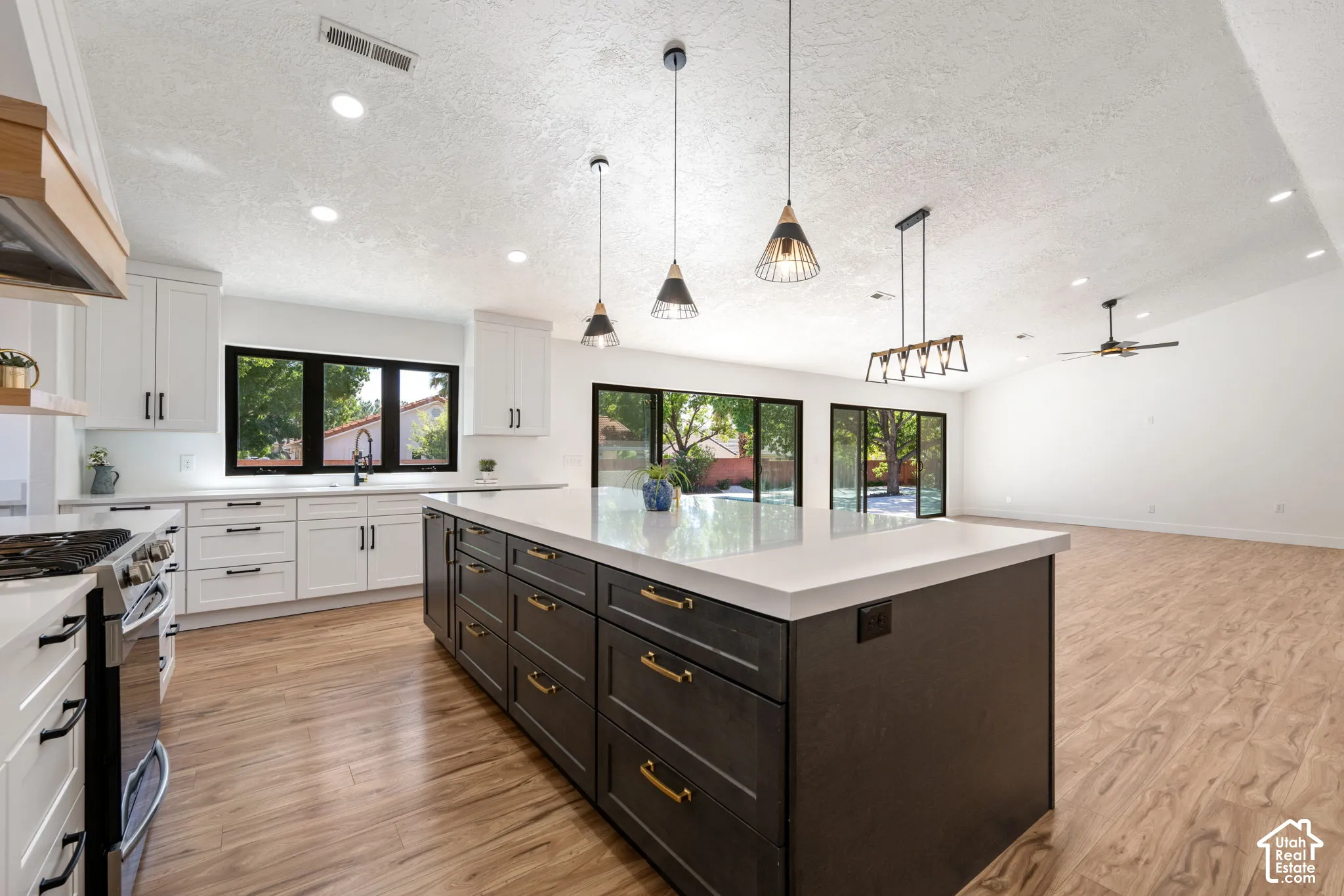 Kitchen featuring a large central island with a light-toned countertop, white cabinetry with dark hardware, wood-finish flooring, and pendant lighting fixtures