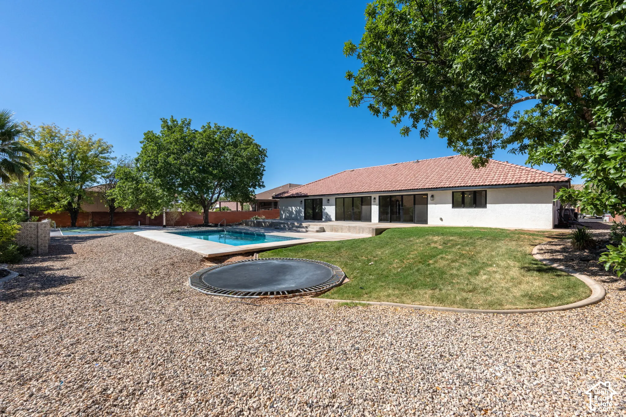 Expansive backyard featuring a rectangular swimming pool, concrete patio, mature trees, and a terraced lawn area